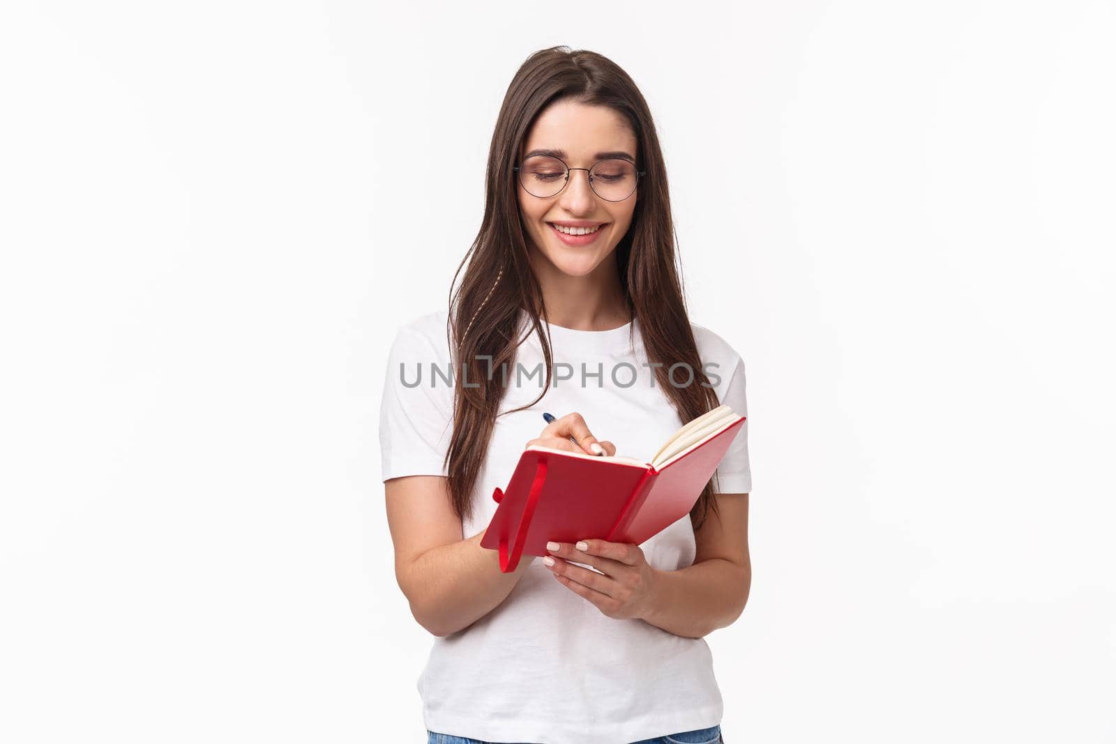 Portrait of smiling pretty caucasian girl writing in her diary, prepare homework for english courses, smiling, have inspiration to write plans for next week in planner, white background.