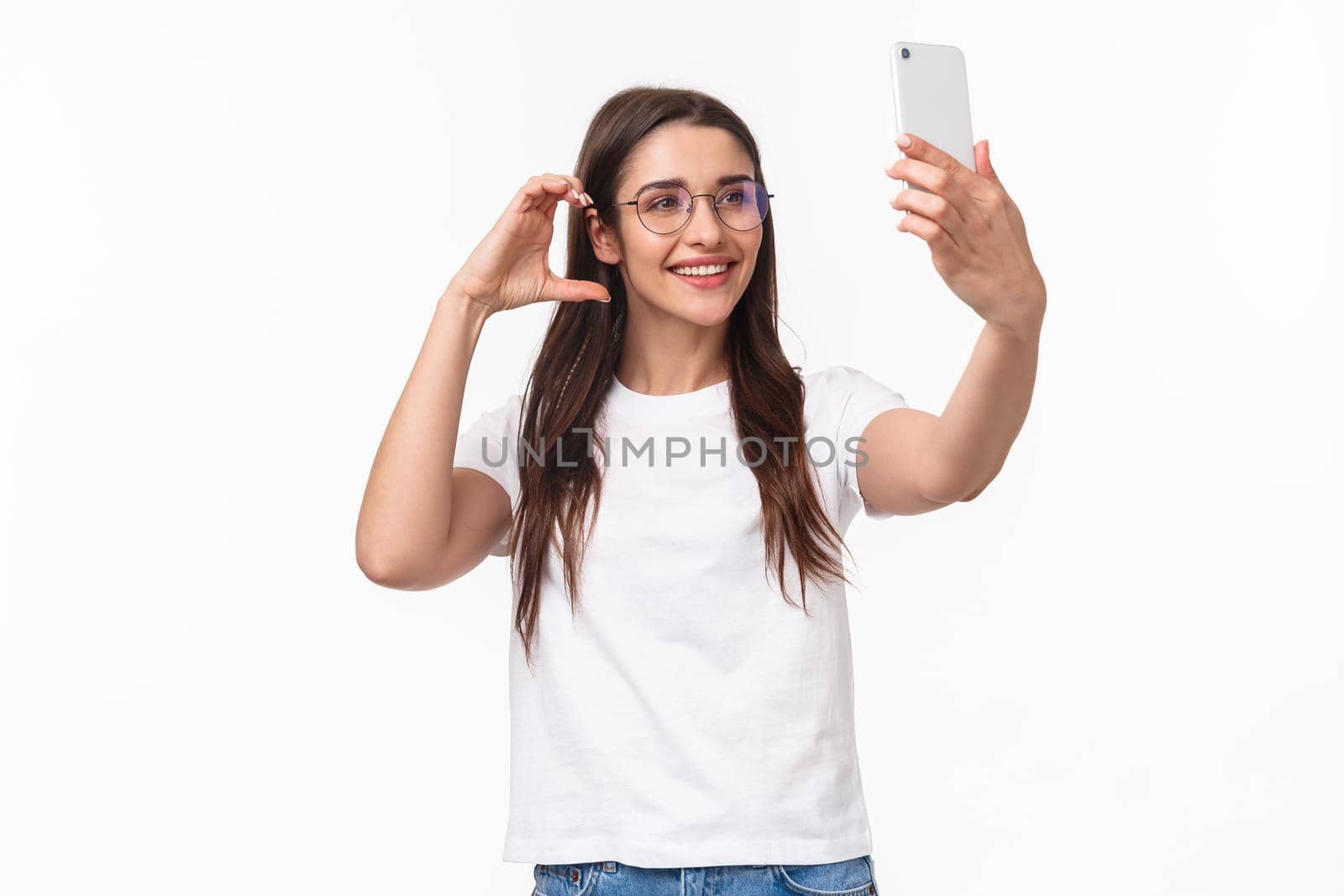 Communication, technology and lifestyle concept. Portrait of charming smiling young woman in glasses, taking selfie on mobile phone trying make pretty cute photo for social media by Benzoix