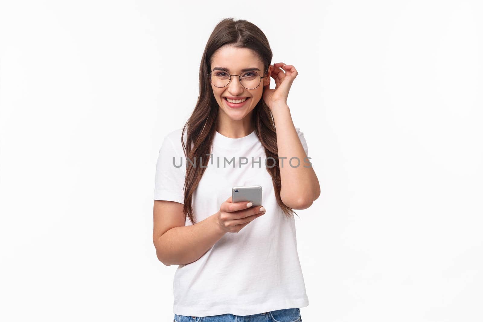 Communication, technology and lifestyle concept. Cute and lovely caucasian woman in t-shirt and glasses, put hair strand behind ear and giggle blushing, receive flirty message, hold mobile phone.