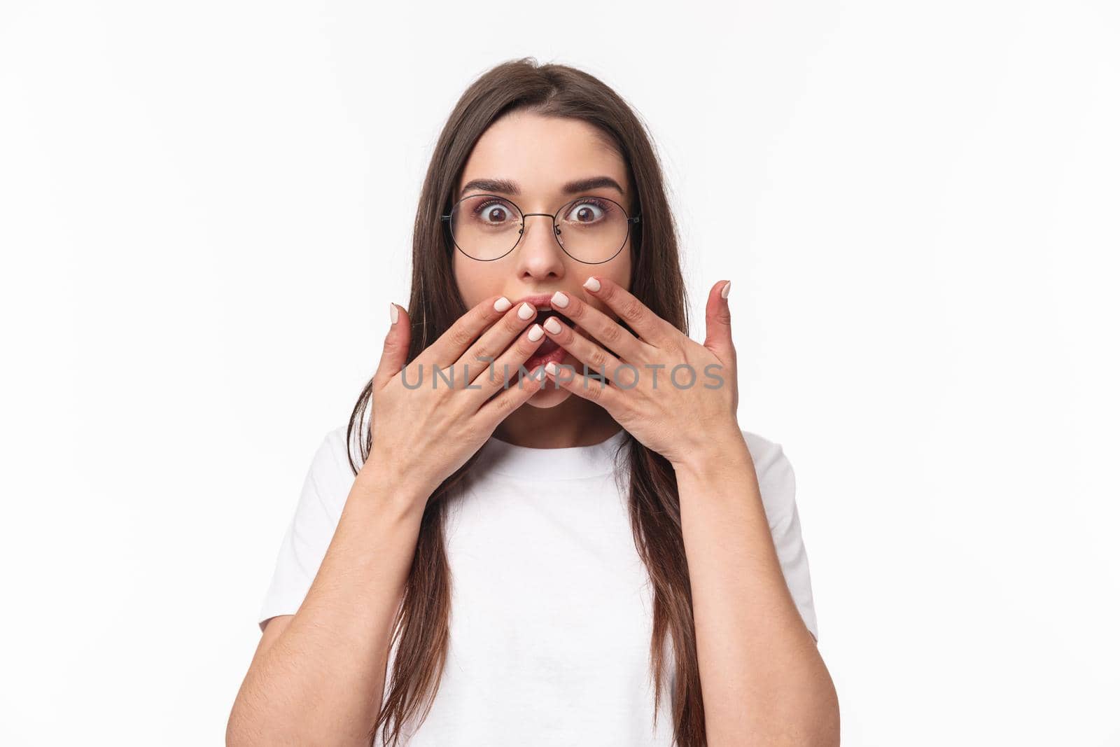 Close-up portrait of enthusiastic, shocked and amazed young happy girl hear awesome gossip, spilled tea, cover opened mouth with palms, express surprise with eyes, white background.