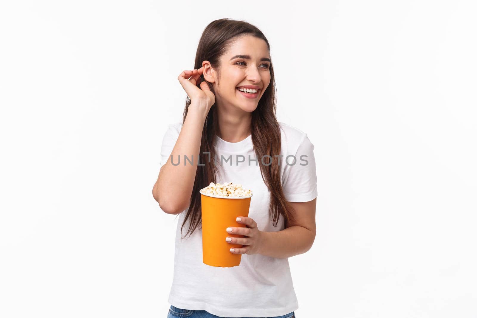 Entertainment, fun and holidays concept. Portrait of beautiful young carefree friendly woman in glasses, place hair strand behind ear giggle joyful watching movie in cinema, eating popcorn.