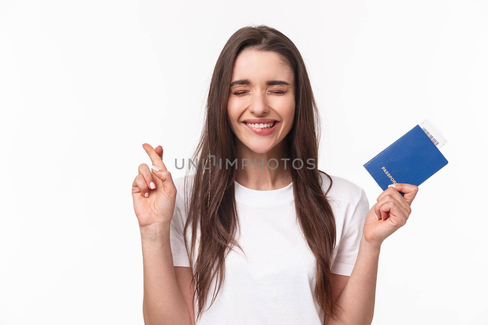 Travelling, holidays, summer concept. Journey beggings. Happy cheerful brunette girl in t-shirt, close eyes and smiling, making wish, cross fingers good luck, holding passport with plane ticket.