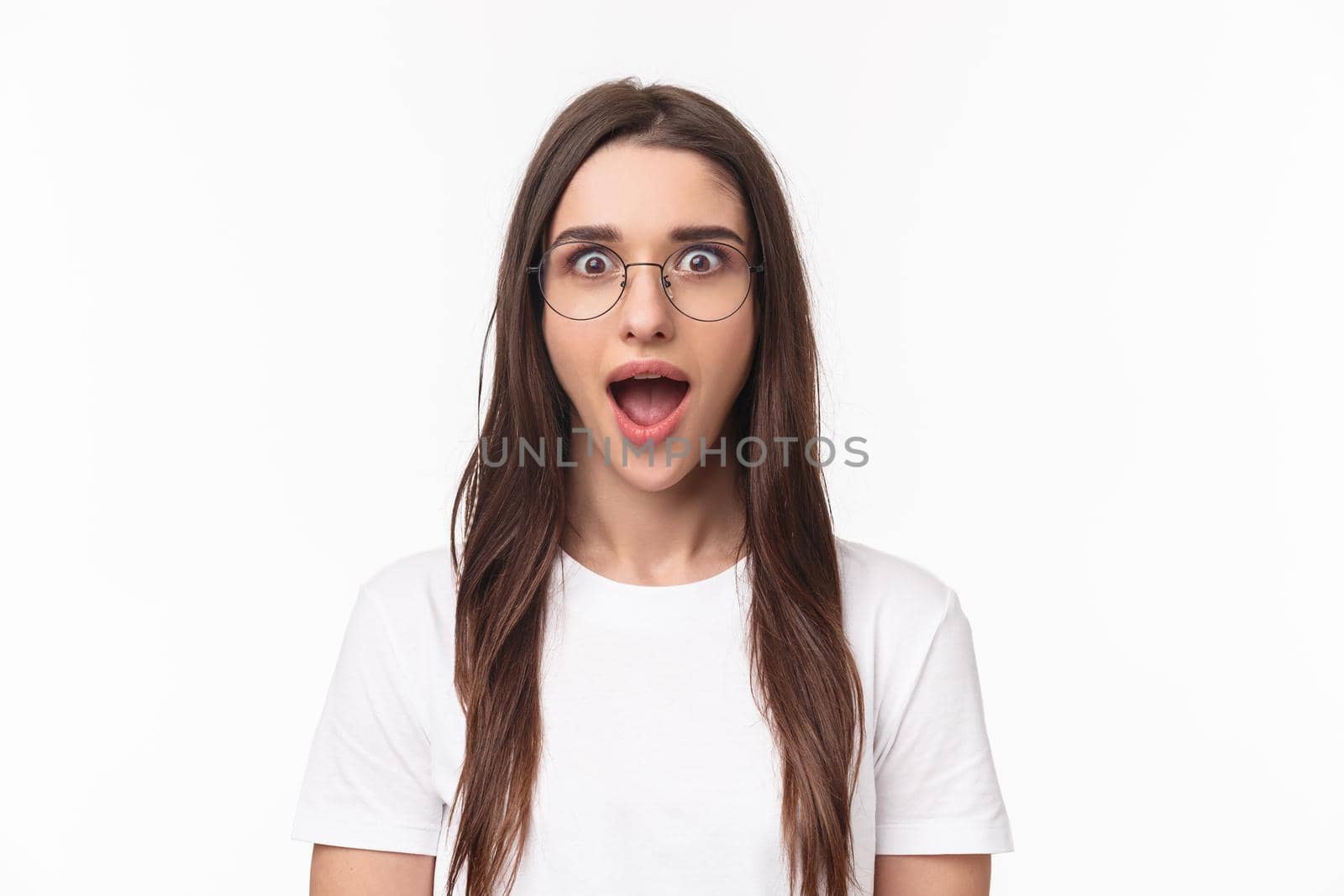 Close-up portrait of enthusiastic, intrigued young brunette woman listening with dropped jaw to amazing news, open mouth fascinated, standing white background, heart great idea, wear glasses by Benzoix