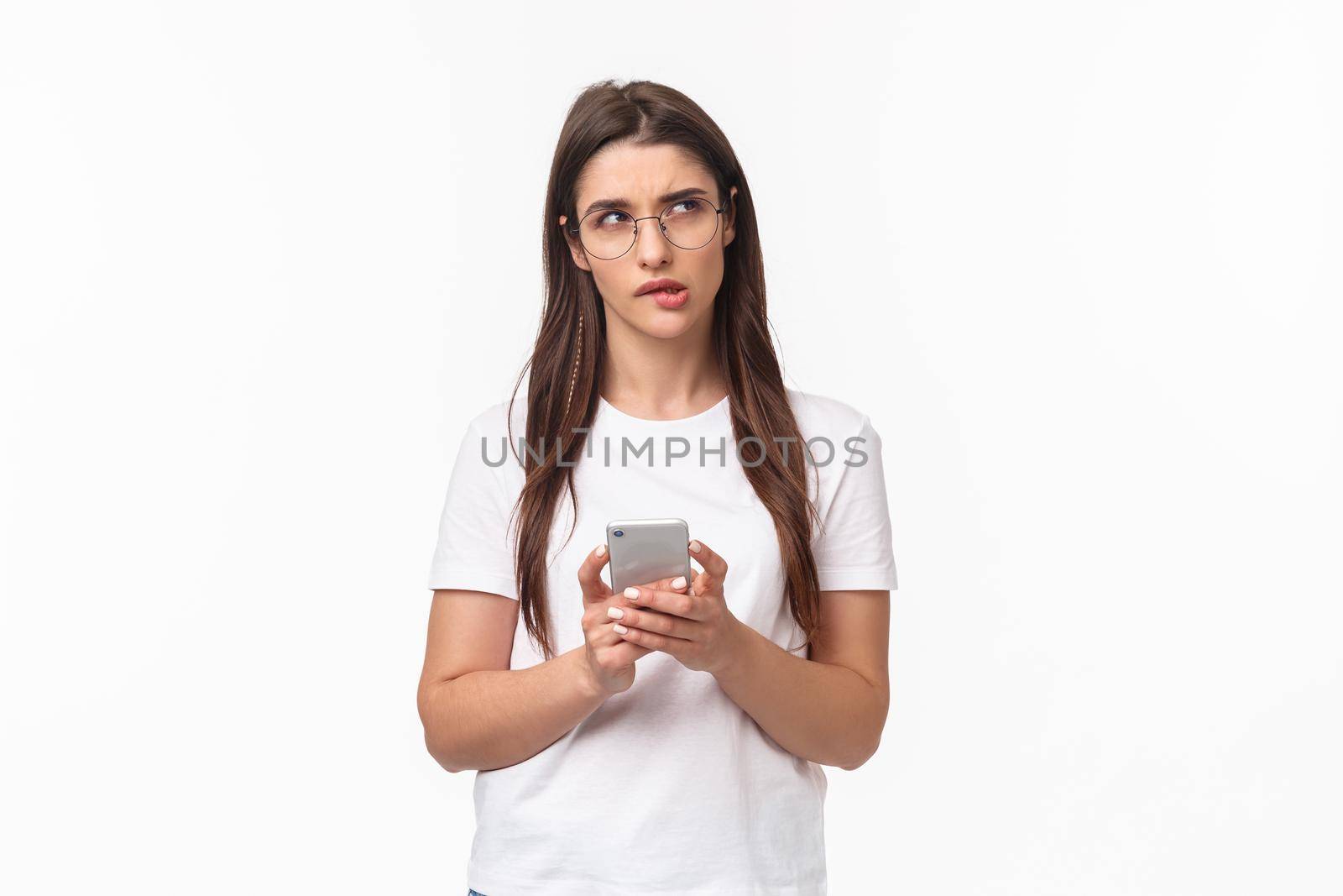 Communication, technology and lifestyle concept. Portrait of thoughtful young woman working remote, answer clients on phone, hold smartphone look up thinking what text back.