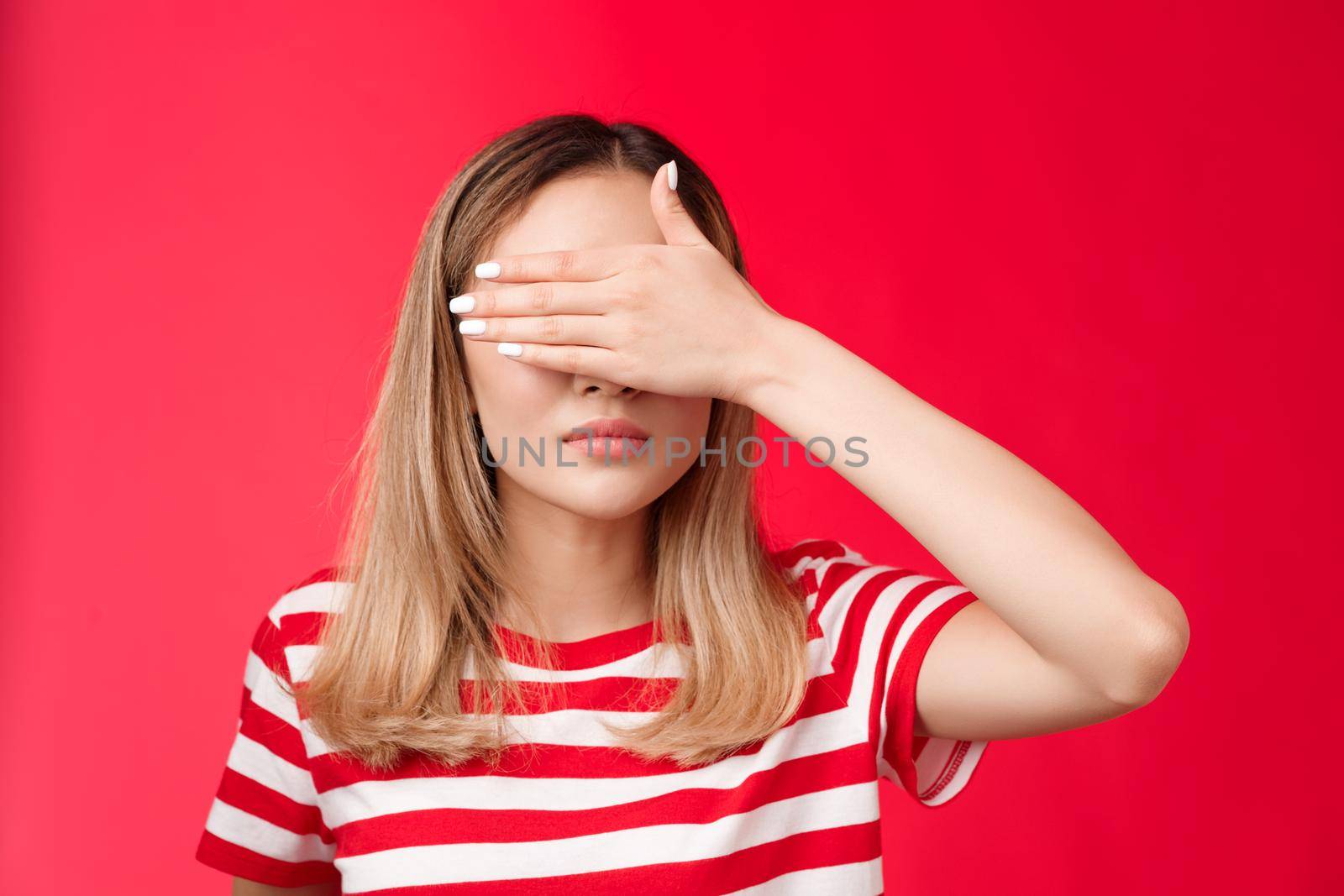 Serious-looking intense asian woman cover sight, hold palm on eyes unwilling see bad scene look focused tensed and pressured standing red background awaiting something happen. Copy space