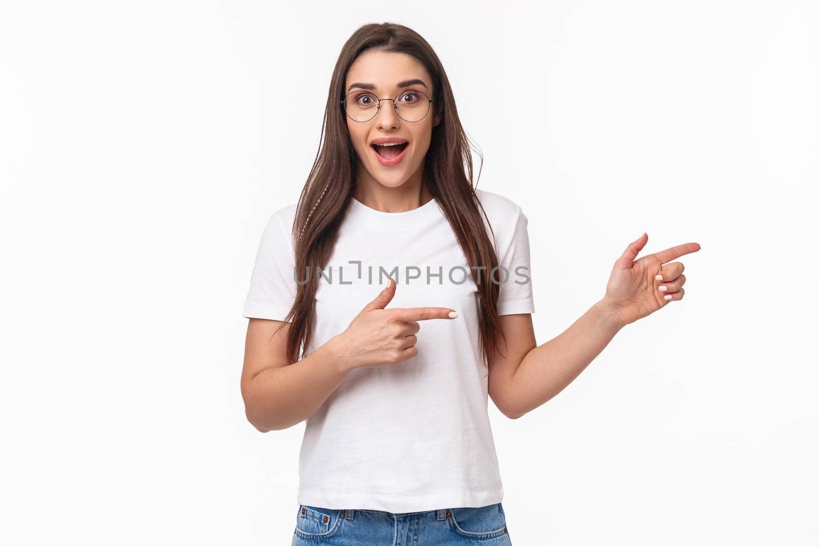 Waist-up portrait of excited, enthusiastic brunette 25s woman in t-shirt, jeans, pointing fingers right and look astonished with amused smile at camera, suggesting visit awesome new place.