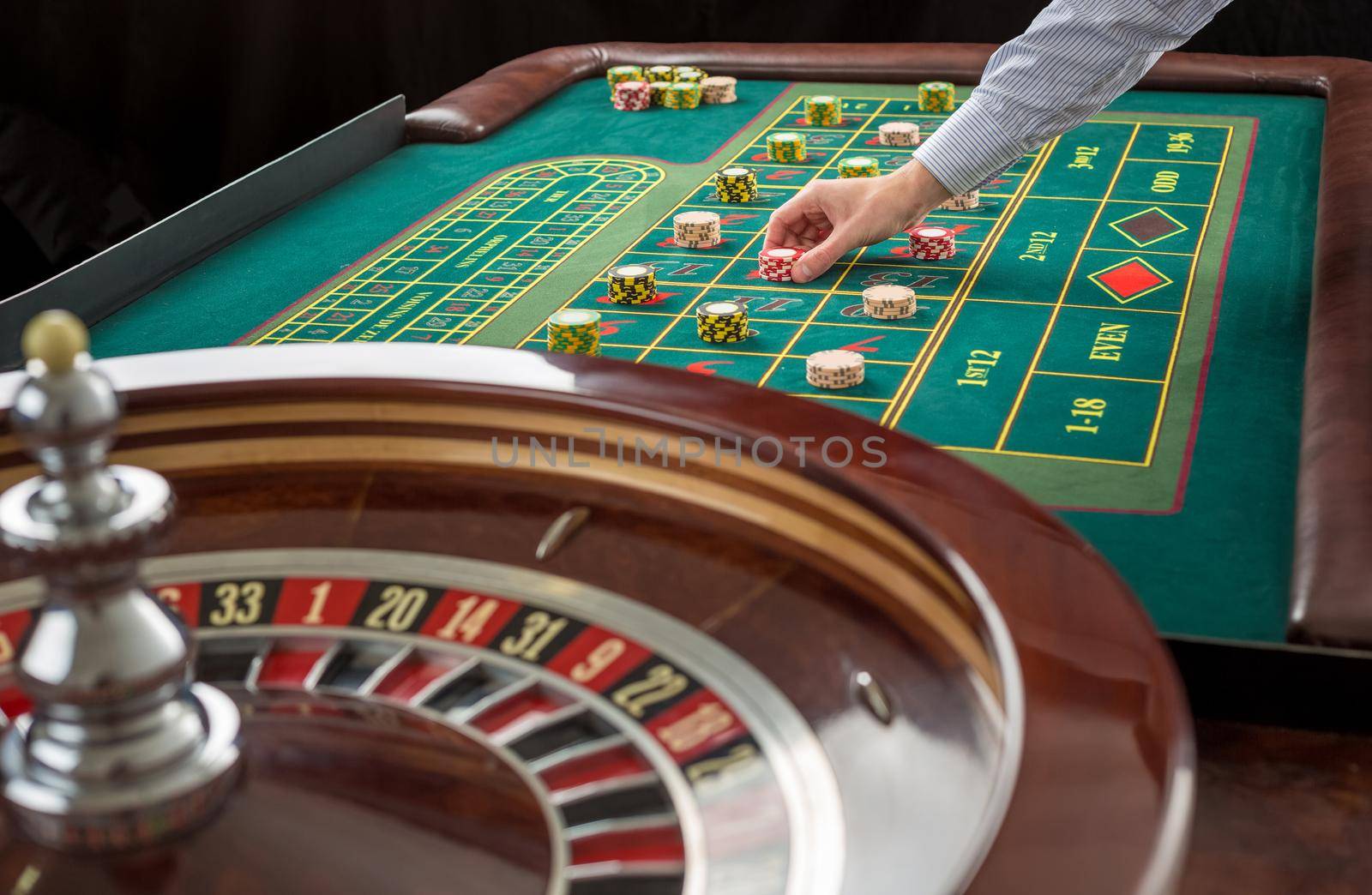 Close up view of Roulette and piles of gambling chips on a green table in casino. Man hand over casino chips on roulette table