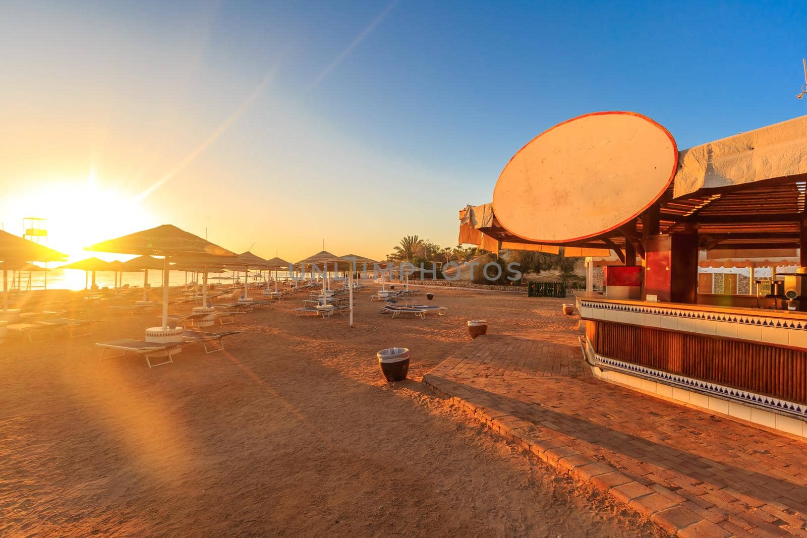 Beach with deck chairs, parasol, and bar at the luxury hotel during sunrise