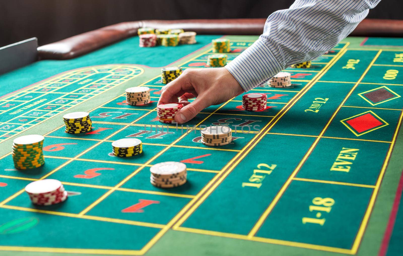 Picture of a green table and betting with chips. Man hand over casino chips on roulette table. Close up