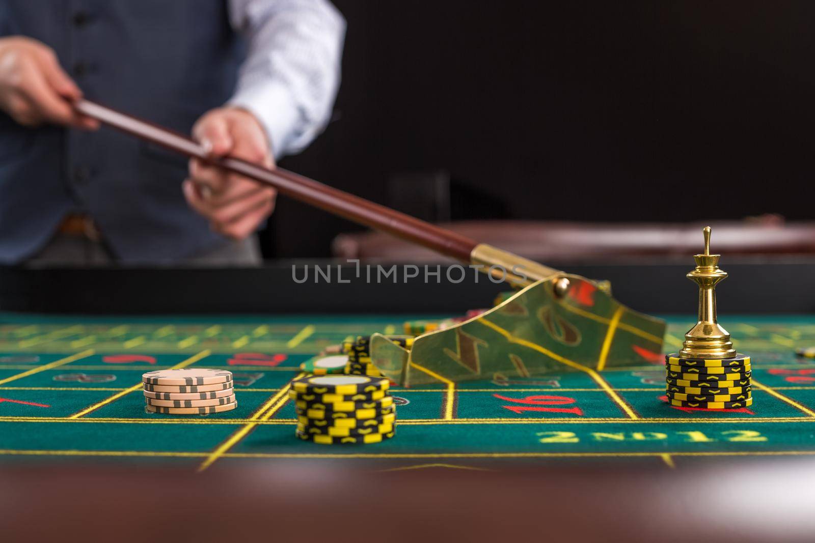 Gambling chips on a green table in casino. Croupier collects chips using stick