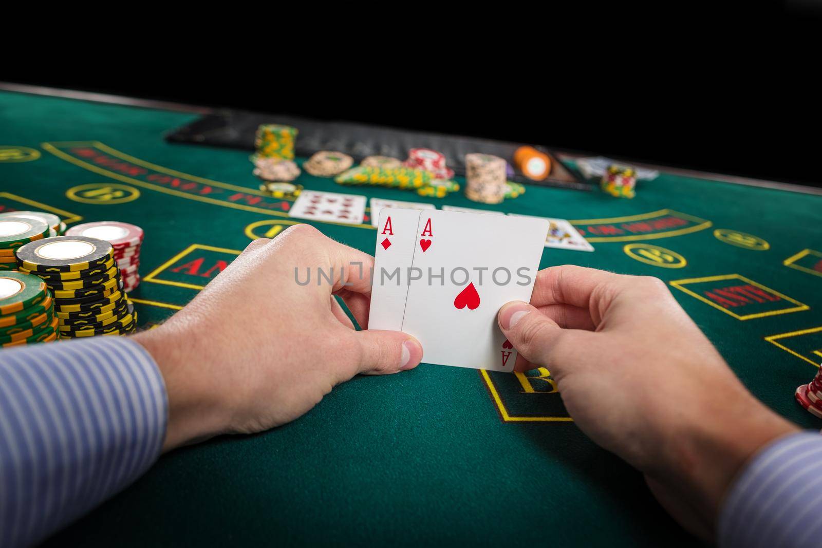 Male poker player holding the of two cards aces at green casino table