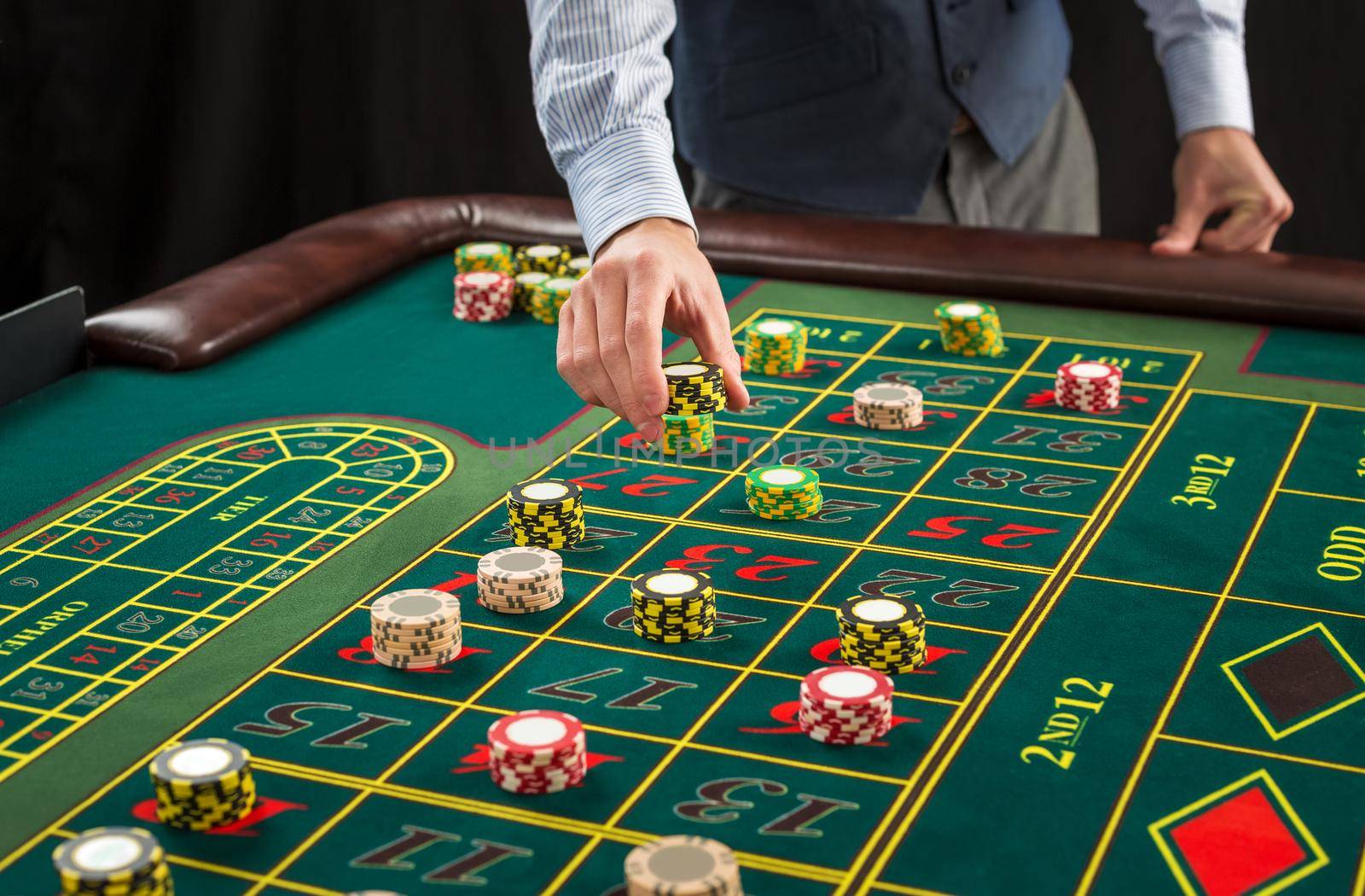 Picture of a green table and betting with chips. Man hand over casino chips on roulette table. Close up