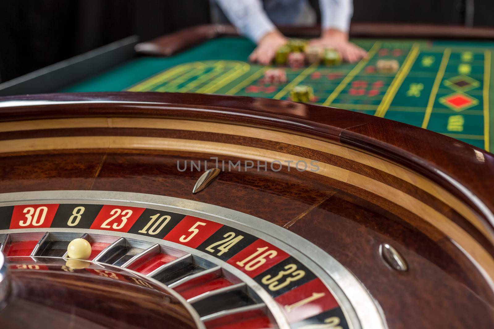 Roulette and piles of gambling chips on a green table in casino. Man hand over casino chips - bet.