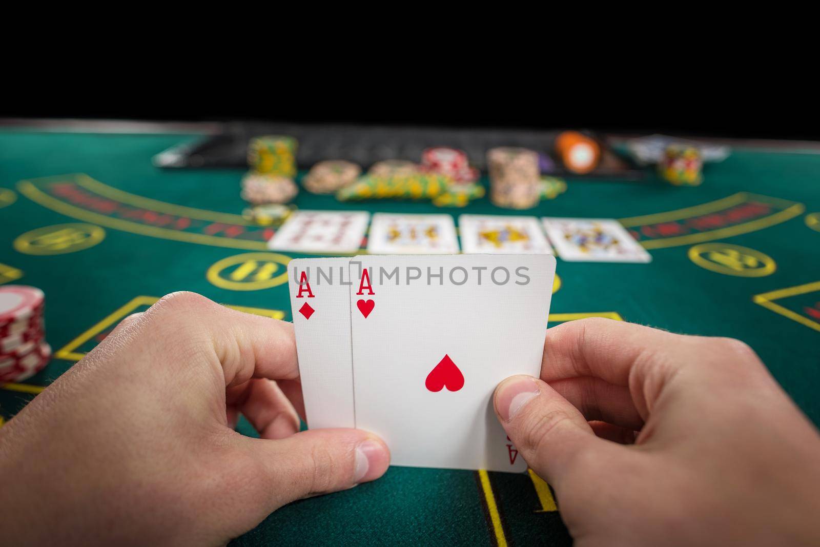 Male poker player holding the of two cards aces at green casino table