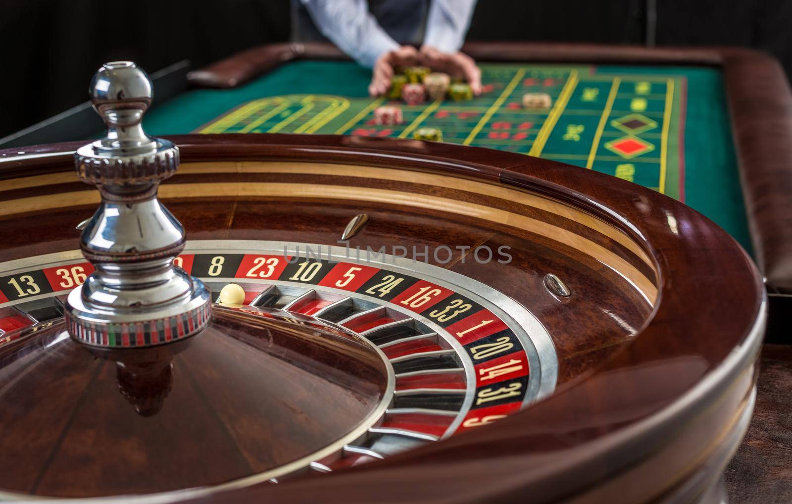 Roulette and piles of gambling chips on a green table in casino. Man hand over casino chips - bet.