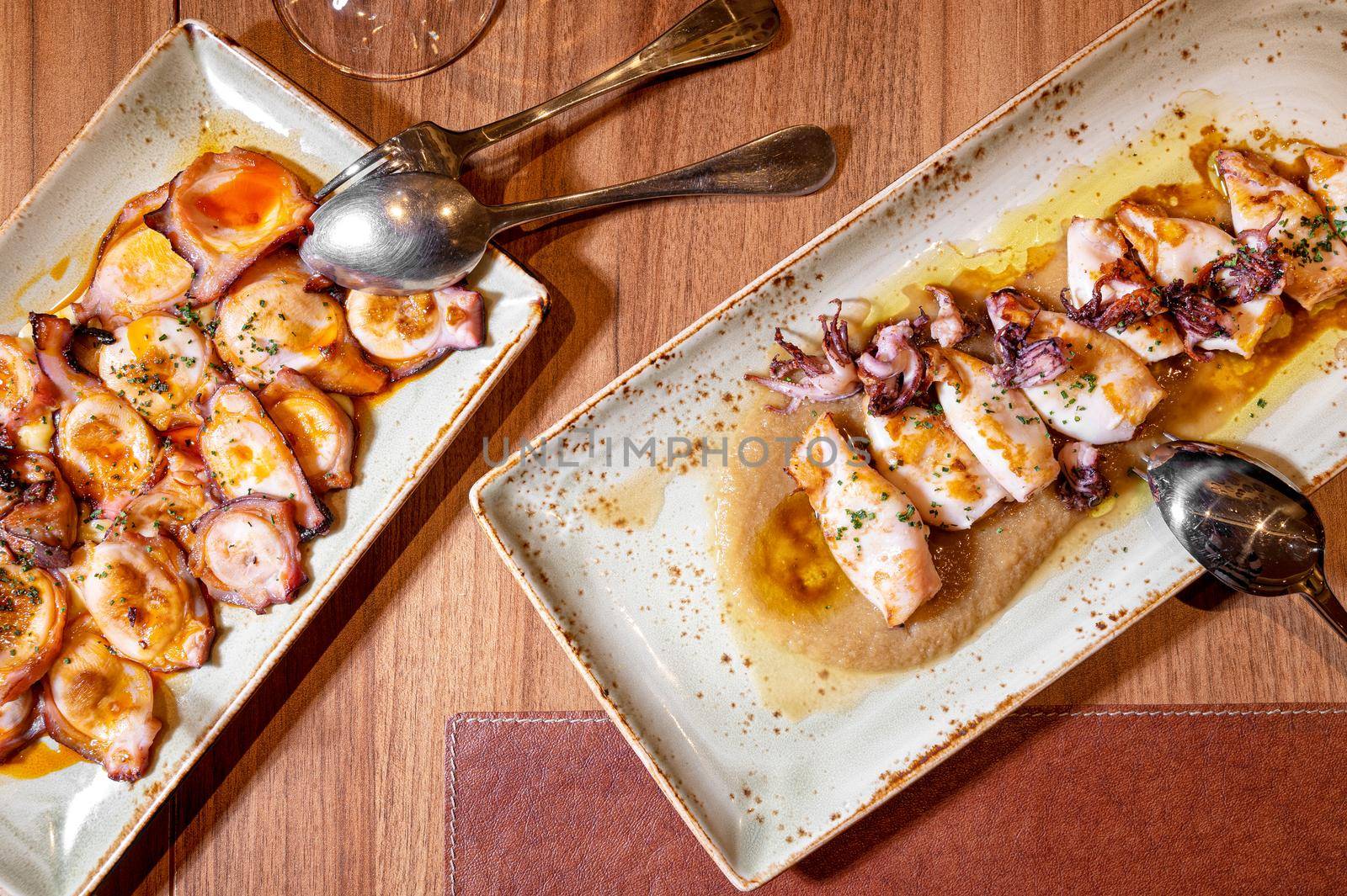 Directly above of a restaurant table with plates of Grilled squid and octopus with olive oil. by HERRAEZ