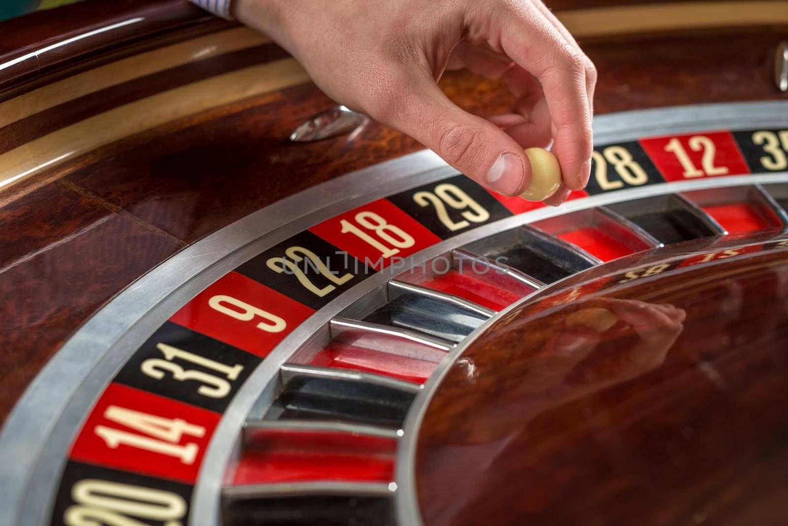 Roulette wheel and croupier hand with white ball in casino close up details