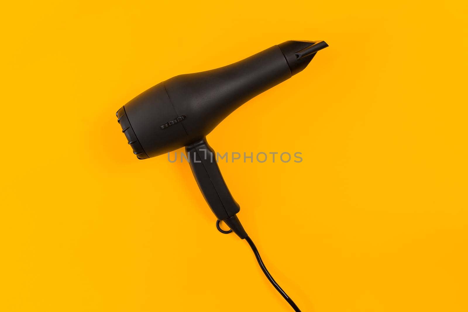 Black hair dryer on yellow paper background. Top view. Copy space. Flat lay. Still life. Mockup