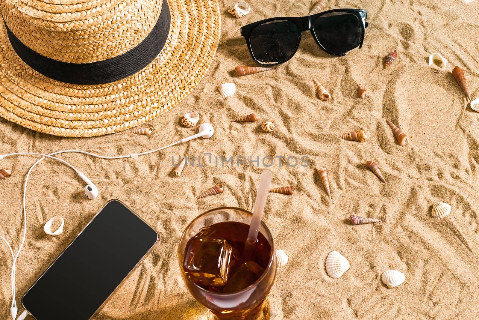Summer beachwear, sunglasses, hat, cold drink in a glass and seashells on sand beach. Top view. Copy space. Still life mockup flat lay