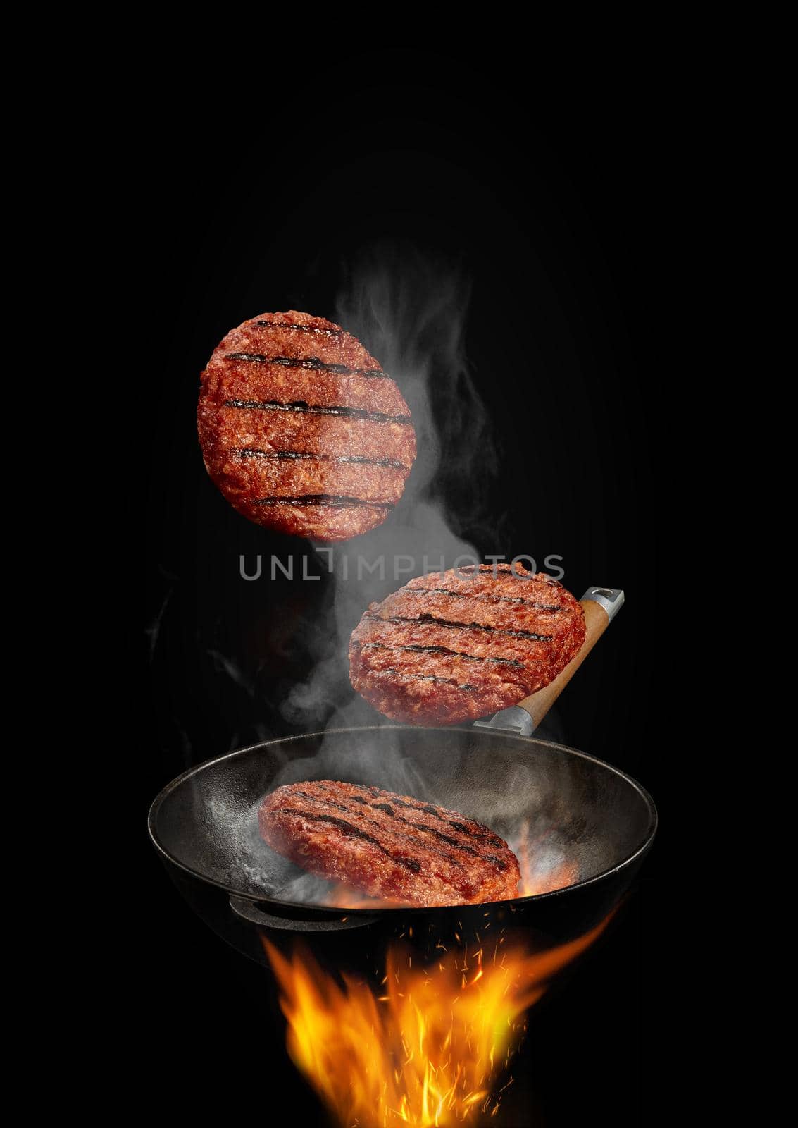 Wok pan with smoke above fire is frying three beef cutlets against black studio background. Cooking concept. Close up by nazarovsergey
