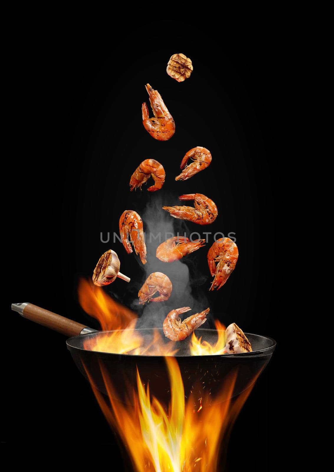 Wok pan with smoke above fire is frying some shrimps with garlic against black studio background. Cooking concept. Close up, copy space