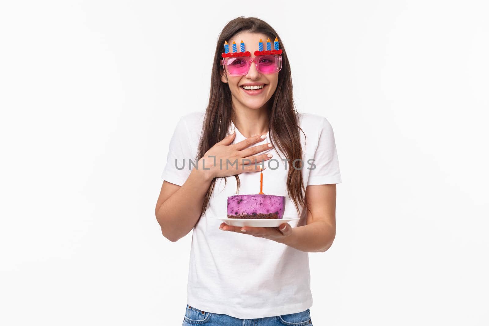 Entertainment, fun and holidays concept. Thankful surprised cute girl celebrating birthday, receive piece cake with lit candle, making b-day wish, wear funny glasses, smiling and laughing happy.
