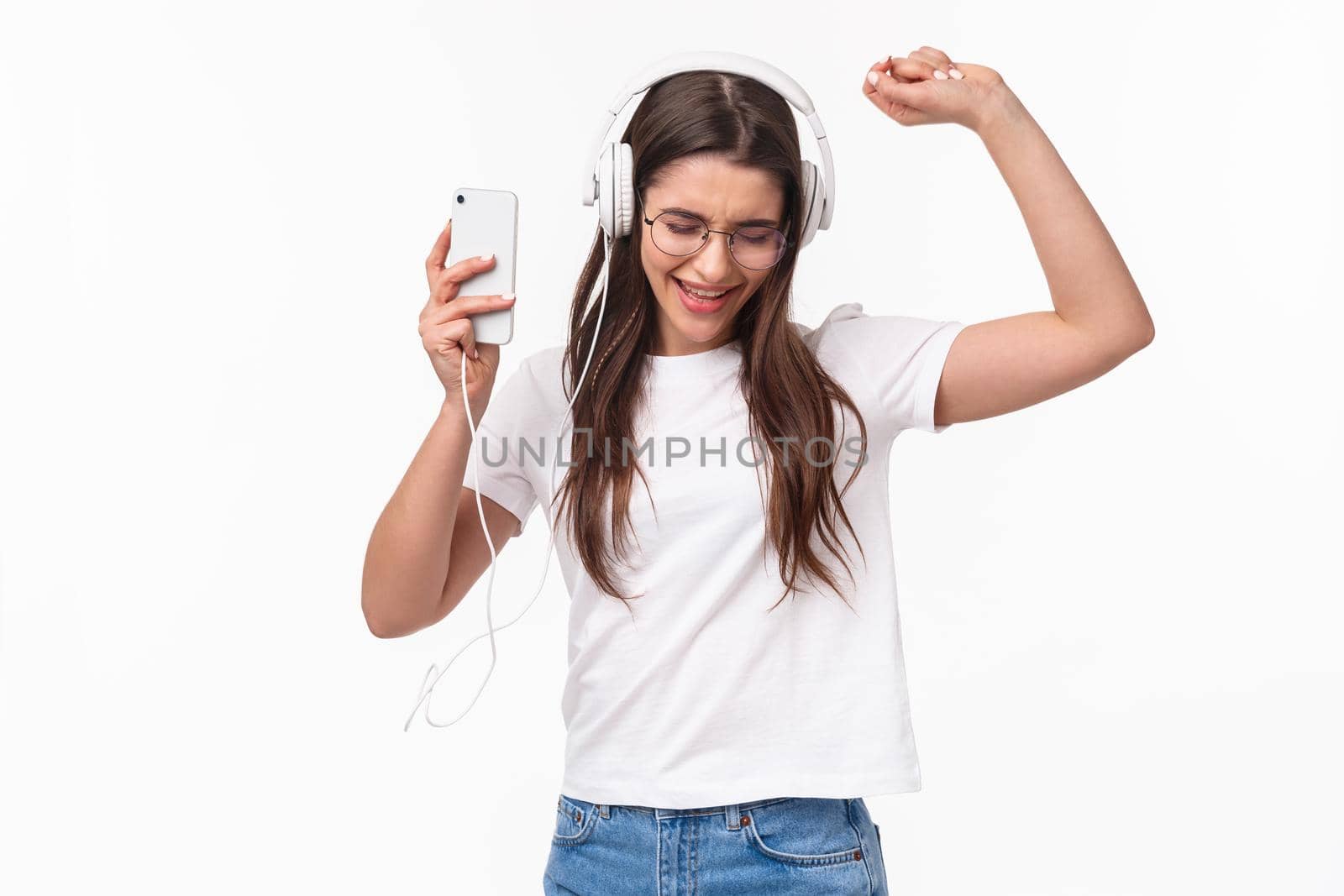 Technology, lifestyle and music concept. Portrait of excited and carefree relaxed beautiful woman having fun listening songs and playlist, vibing dancing alone in headphones, hold mobile phone by Benzoix