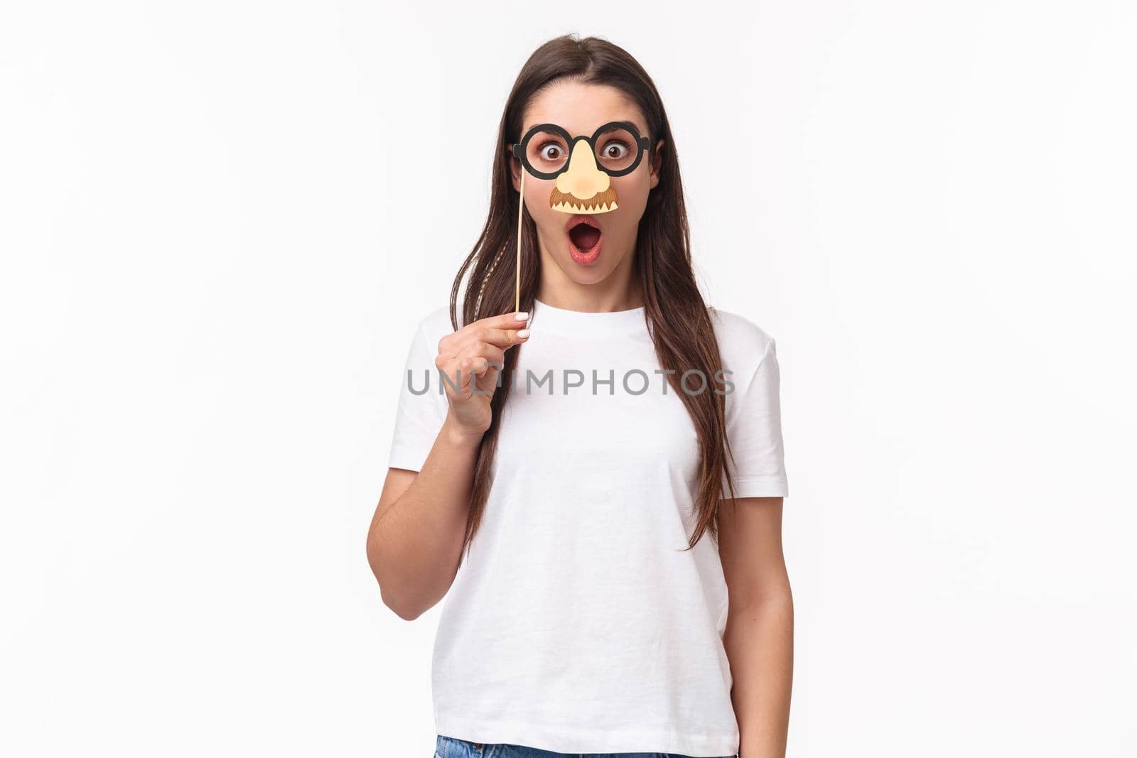 Entertainment, fun and holidays concept. Funny and cute young girl fool around, praying wearing glasses and nose mask, gasping amazed, look surprised standing white background.