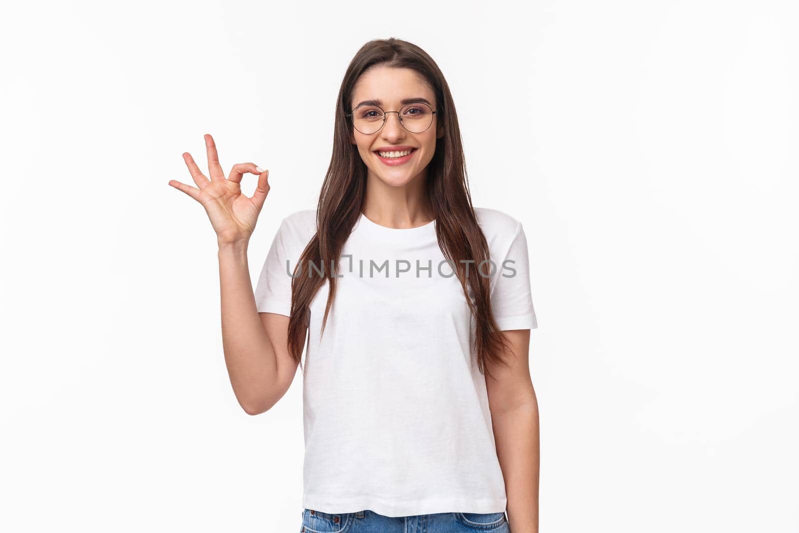 Waist-up portrait of optimistic, smiling happy young pretty woman in glasses, showing okay sign, agree or recommend something, give positive review, approve excellent choice, white background.