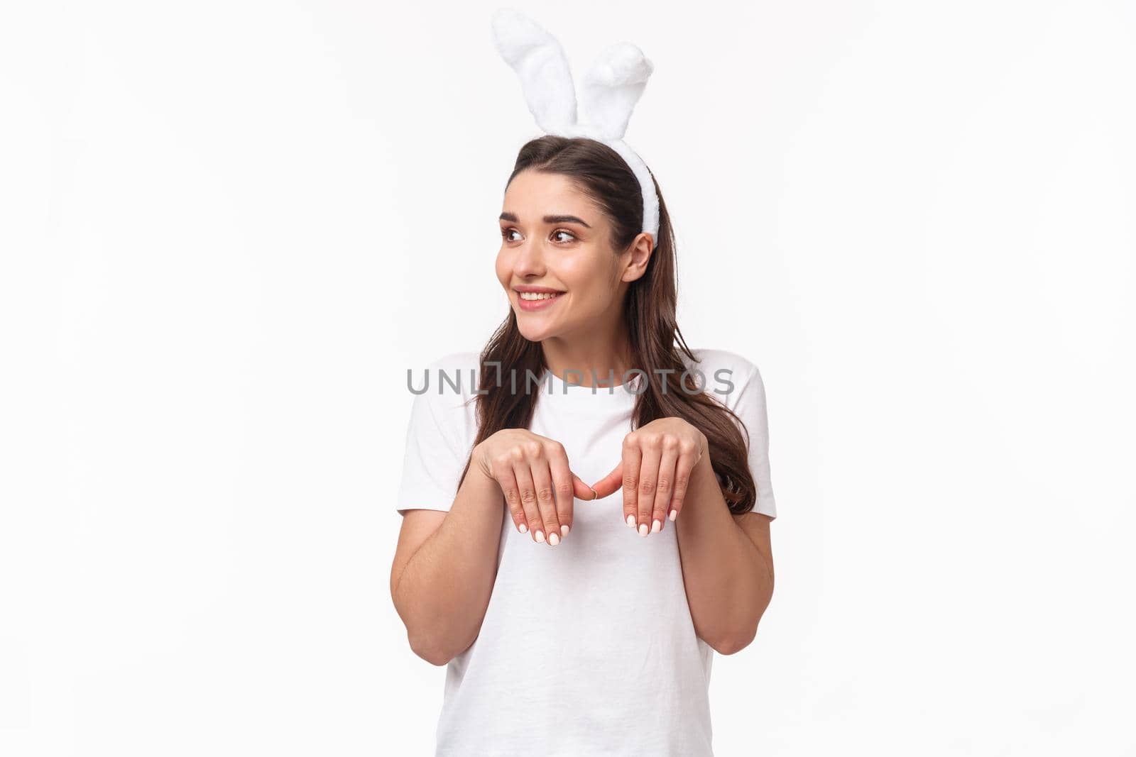 Portrait of funny and cute, playful adult girl in t-shirt and rabbit ears, look away with amused happy face, imitating bunny with paws and silly grin, look away, standing white background by Benzoix