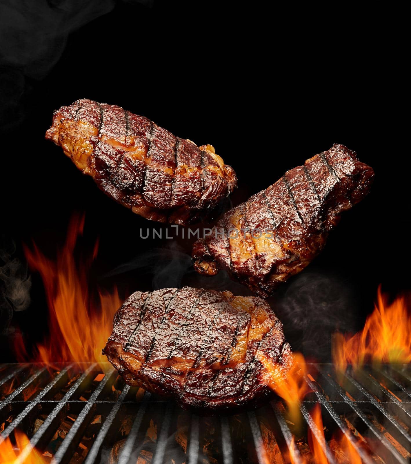 Delicious grilled pork or beef steaks are falling down on black background. Barbecue bbq grill, flaming fire, ember charcoal and smoke. Close up by nazarovsergey