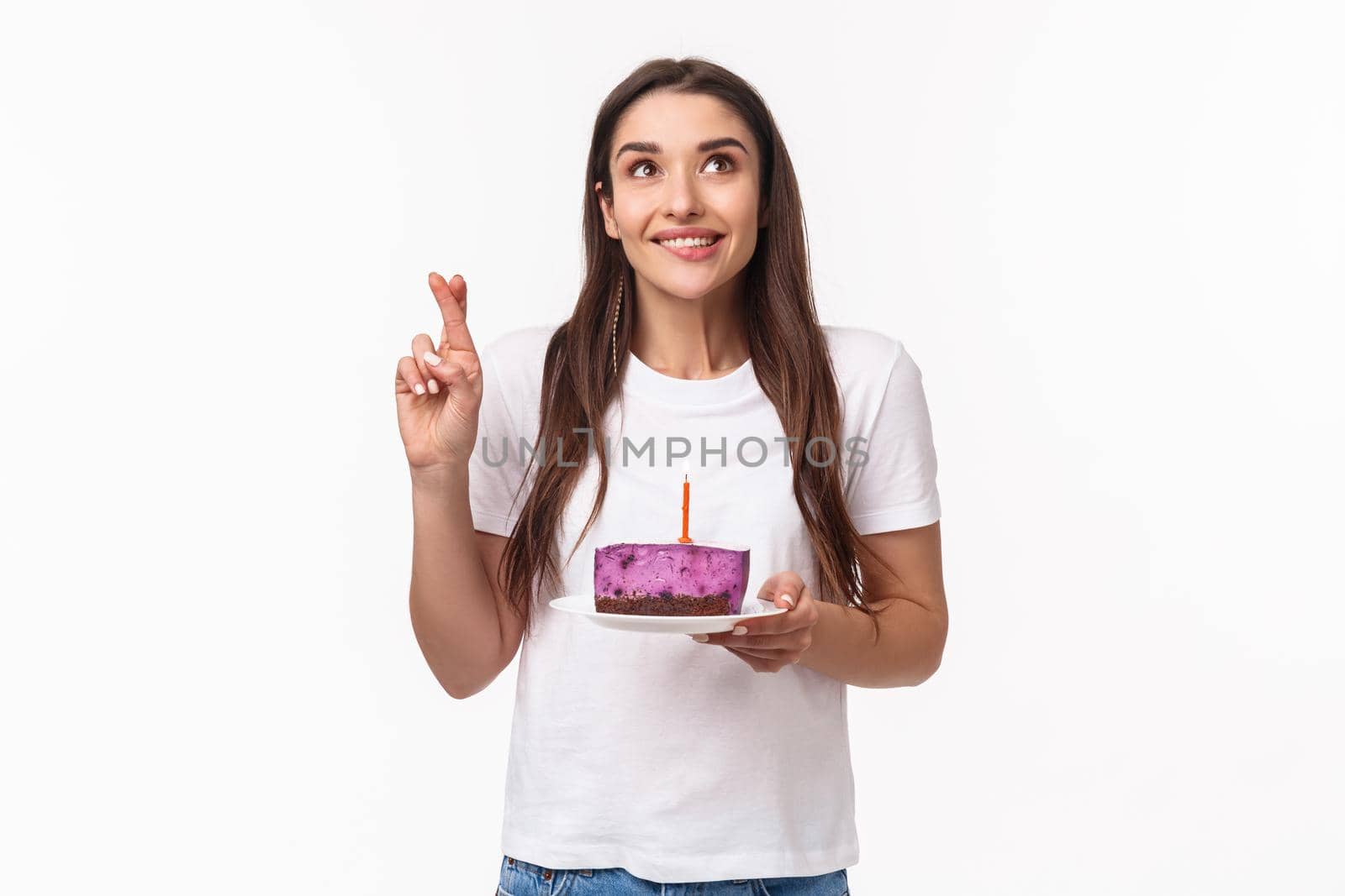 Entertainment, fun and holidays concept. Portrait of positive, smiling wishful young girl, cross finger good luck, bite lip eager wish come true, smiling up at blowing candle on birthday cake by Benzoix