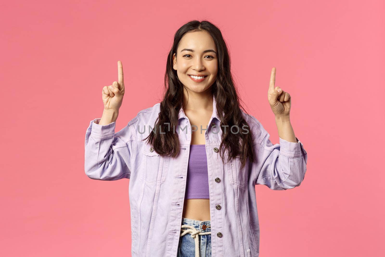 Spring, fashion and people concept. Cheerful young pretty girl in denim jacket, pointing fingers up as showing advertisement, beaming smile camera, inviting to click link, follow or subscribe by Benzoix
