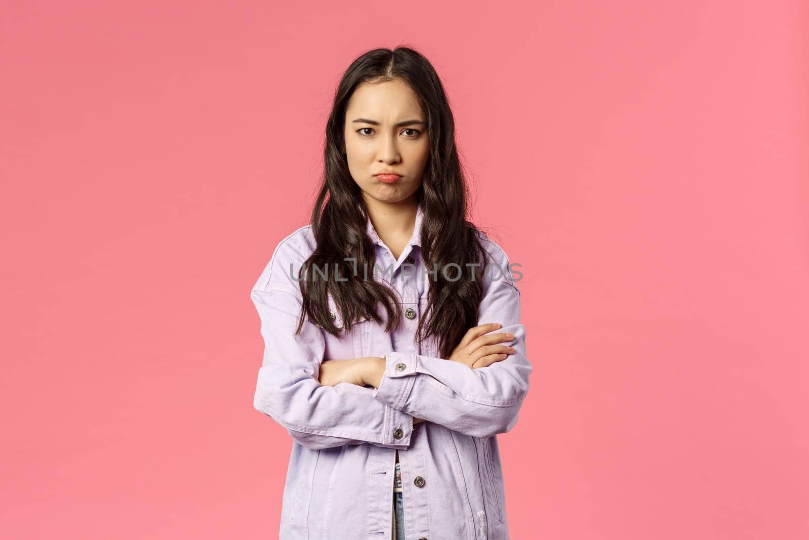 Portrait of gloomy offended young defensive girl, cross hands over chest frowning and sulking, feel betrayed or insulted, unwilling to speak with friend, standing pink background reluctant.