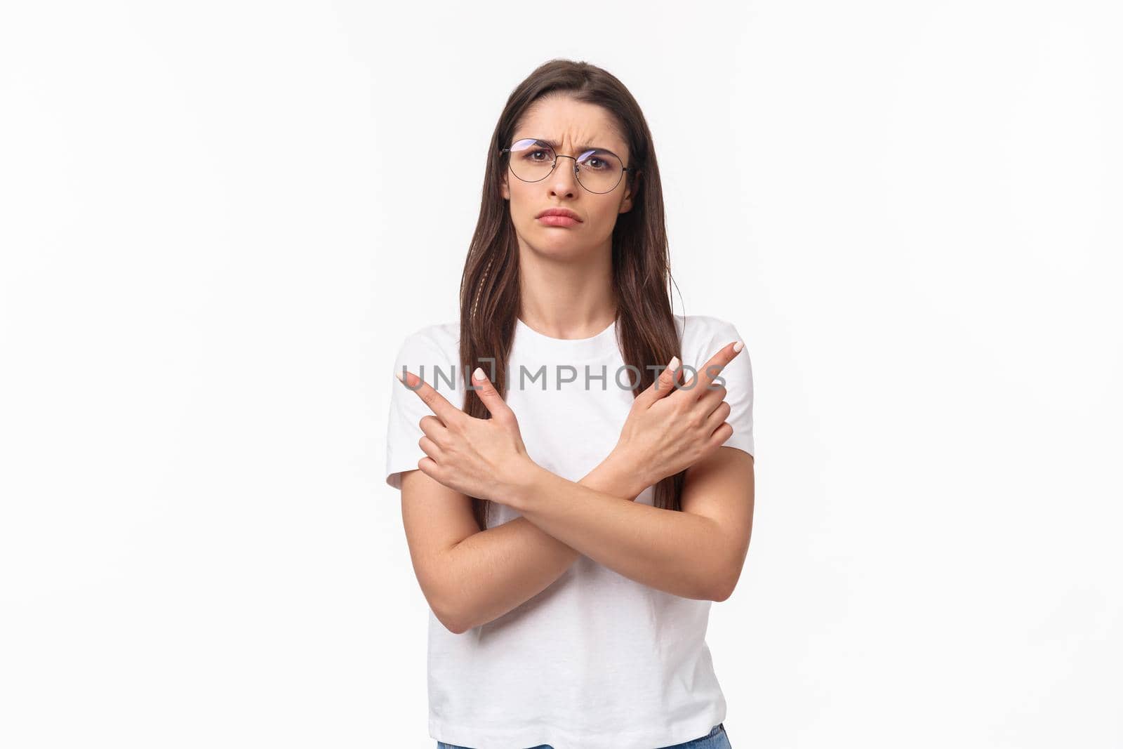 Waist-up portrait of indecisive, puzzled and confused good-looking young woman in glasses, t-shirt, cross hands pointing finger left and right at two variants, frowning, cant decide, white background.