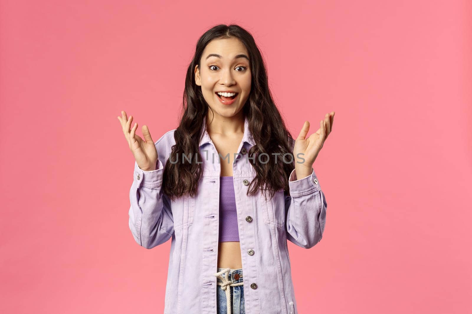 Portrait of surprised, enthusiastic korean girl in denim jacket, look wondered and happy, hear great news, applause, raise hands to clap and praise great work, smiling joyfully, pink background.