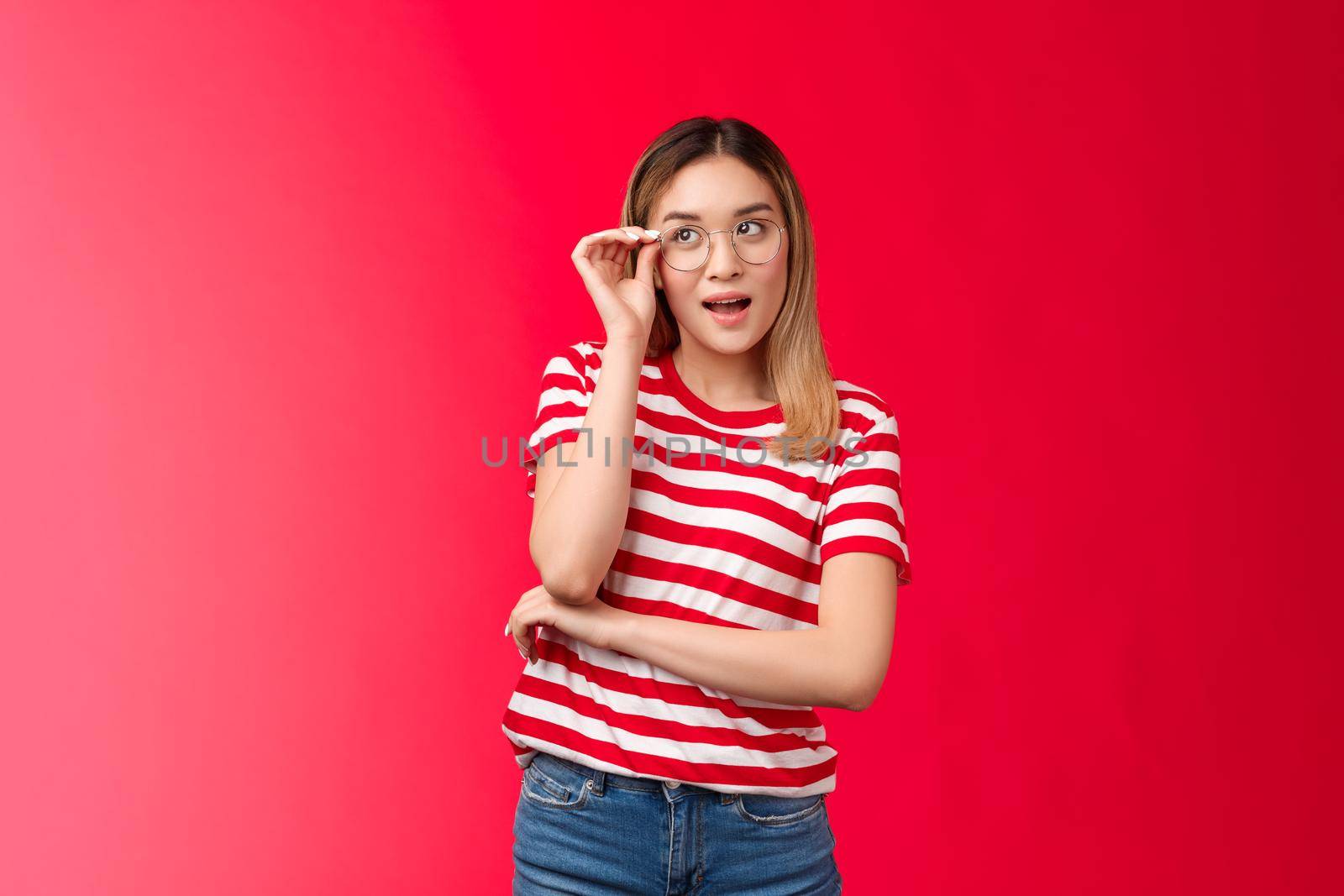 Attractive creative blond asian female journalist got great idea wear glasses check eyewear nose look up intrigued, pondering plan making assumptions, stand red background curious and intrigued by Benzoix