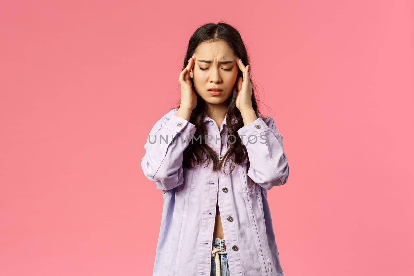 Health, people and lifestyle concept. Girl having troubles, feeling headache cant focus on work as suffer huge migraine, usual painkillers dont work, close eyes and touch temples, pink background.