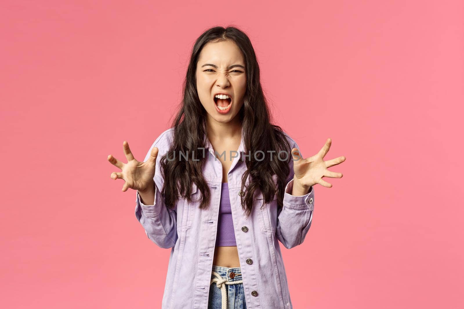 Portrait of aggressive young bothered girl losing temper, screaming furious and angry grimacing, yelling at person with hate and aggression, squeeze hands into fists, pissed-off, pink background.