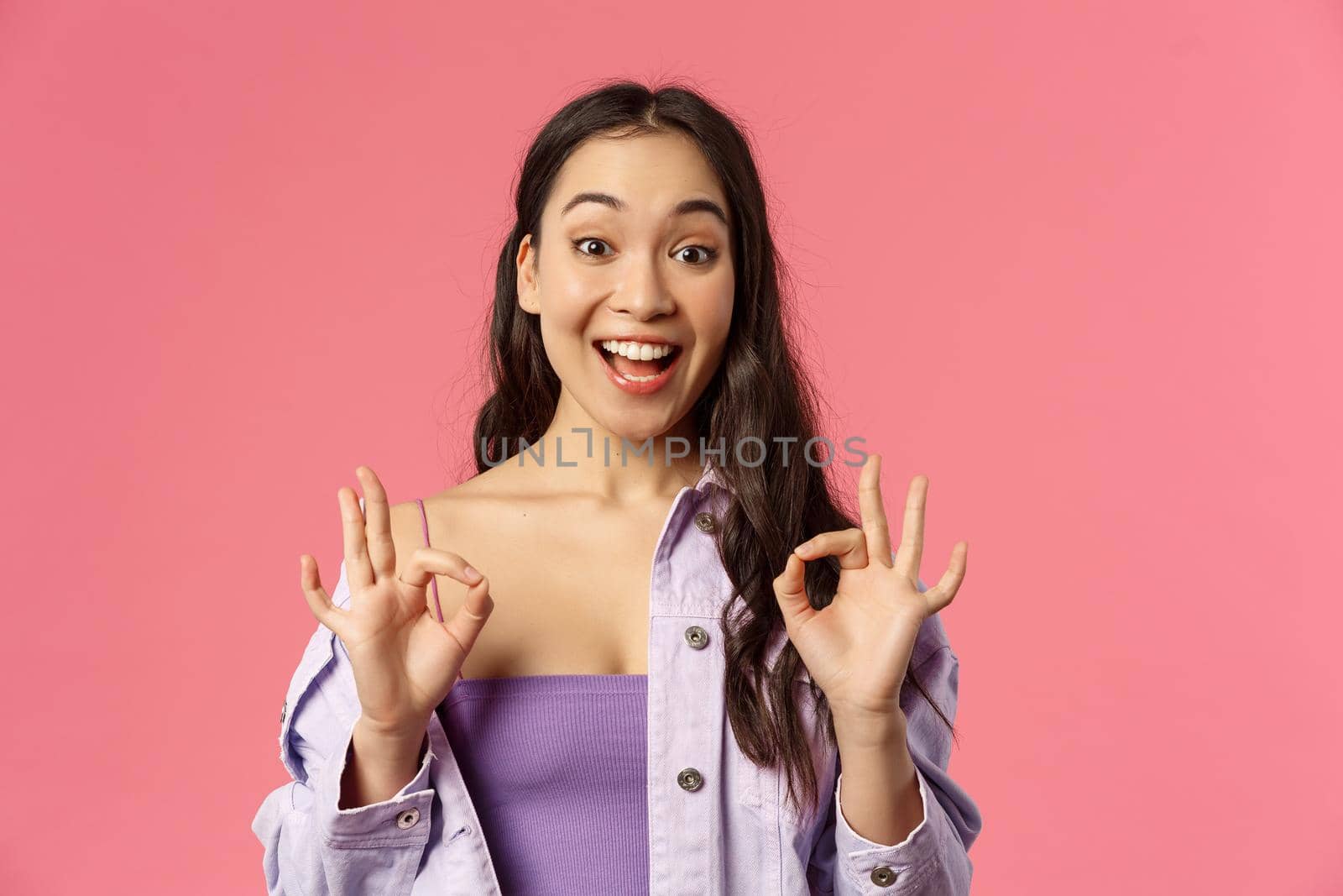 Excellent choice. Close-up portrait of happy amused young stylish asian girl satisfied, showing okay signs and smiling, nod in approval, totally agree, think product super cool, pink background.