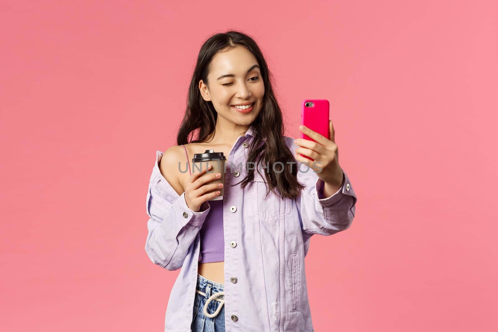 Start your day right. Portrait of good-looking enthusiastic young asian girl in stylish outfit, taking selfie with take-away coffee, recommend followers great cafe to grab drink, pink background by Benzoix