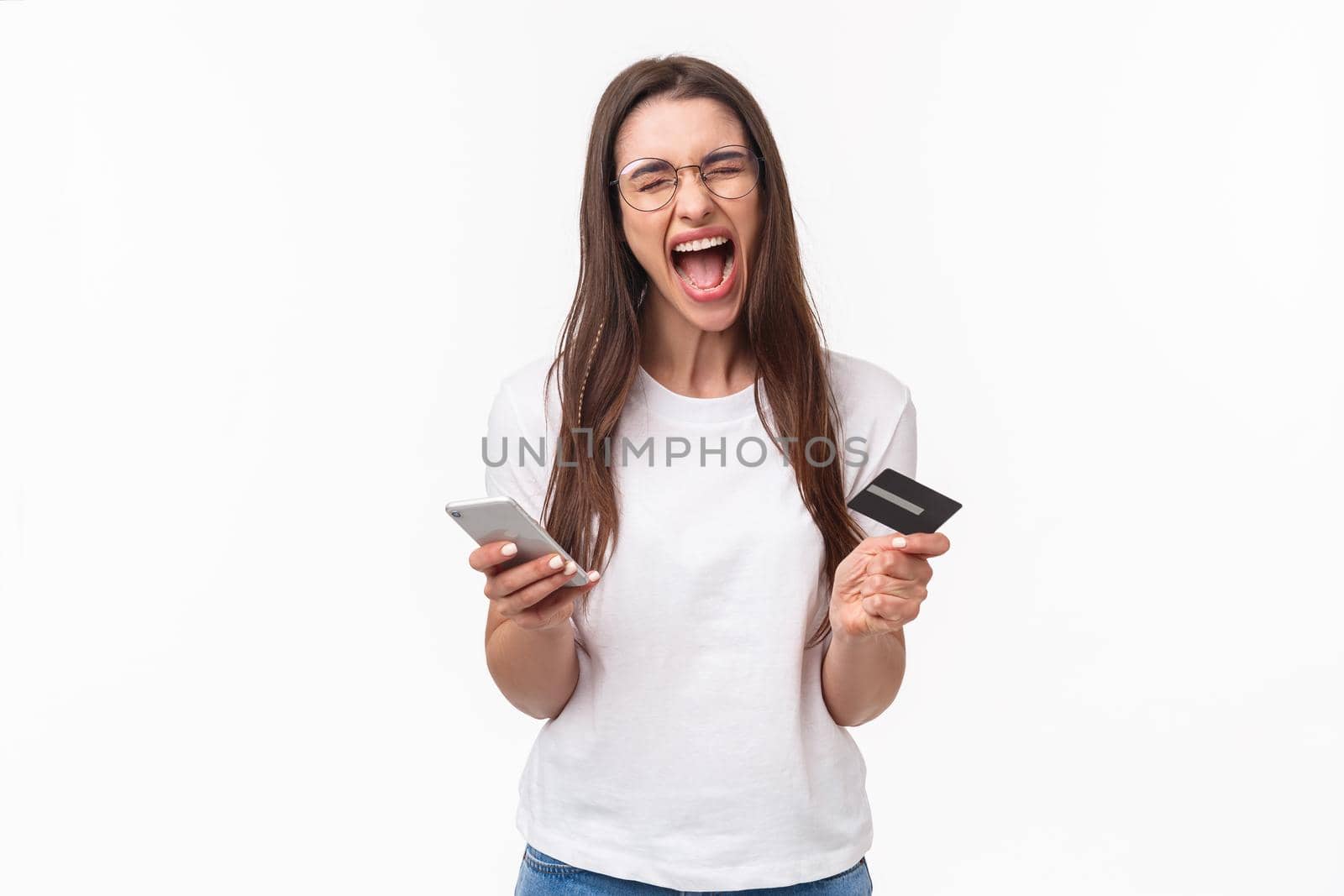 Portrait of uneasy annoyed and angry young brunette female in t-shirt yelling pissed-off as checking bank account, have no money on credit card, or it expired, hold mobile phone, white background by Benzoix