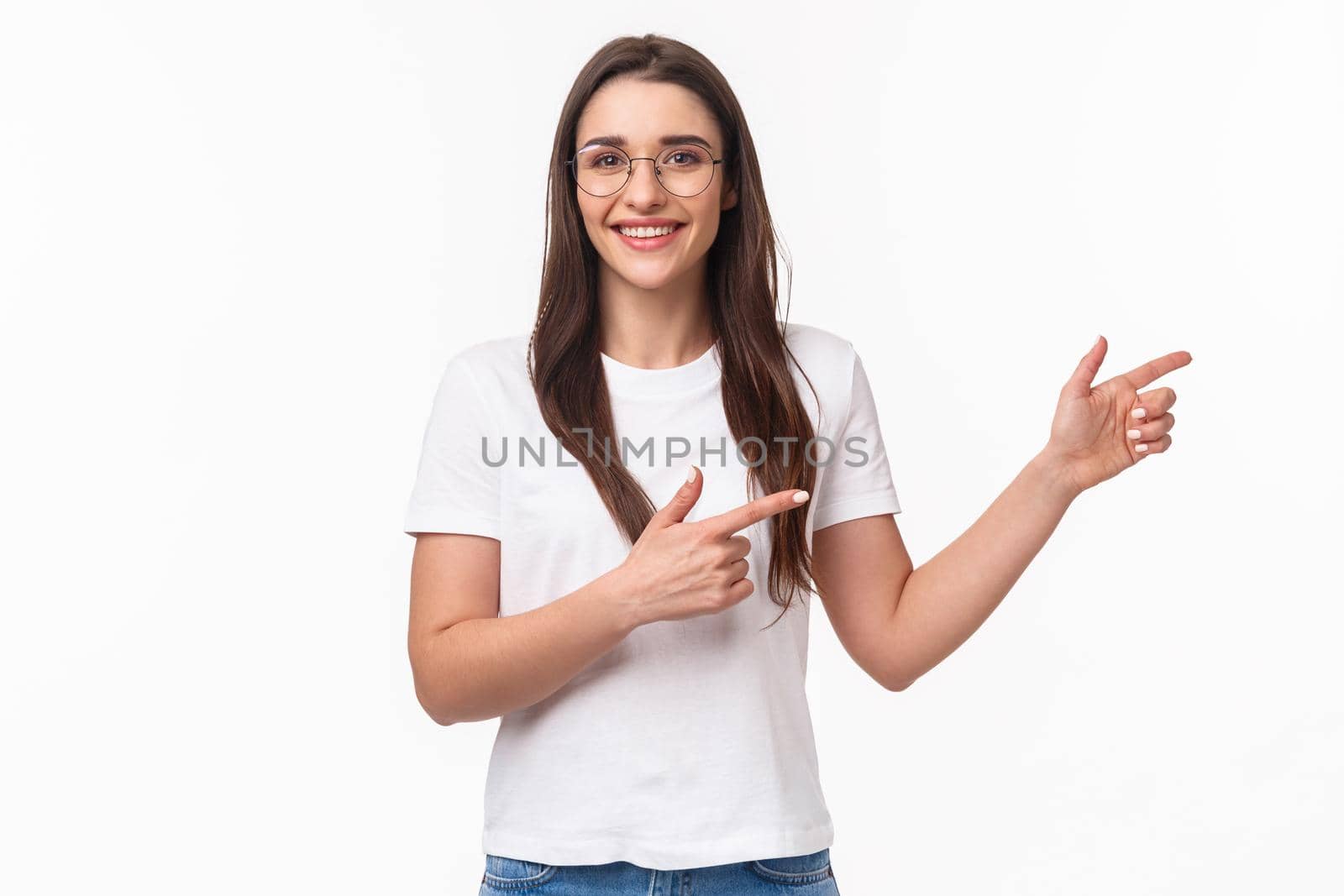 Waist-up portrait of enthusiastic, pleasant brunette woman in glasses inviting check out promo, visit or click link, pointing fingers right and smiling at camera, standing white background by Benzoix