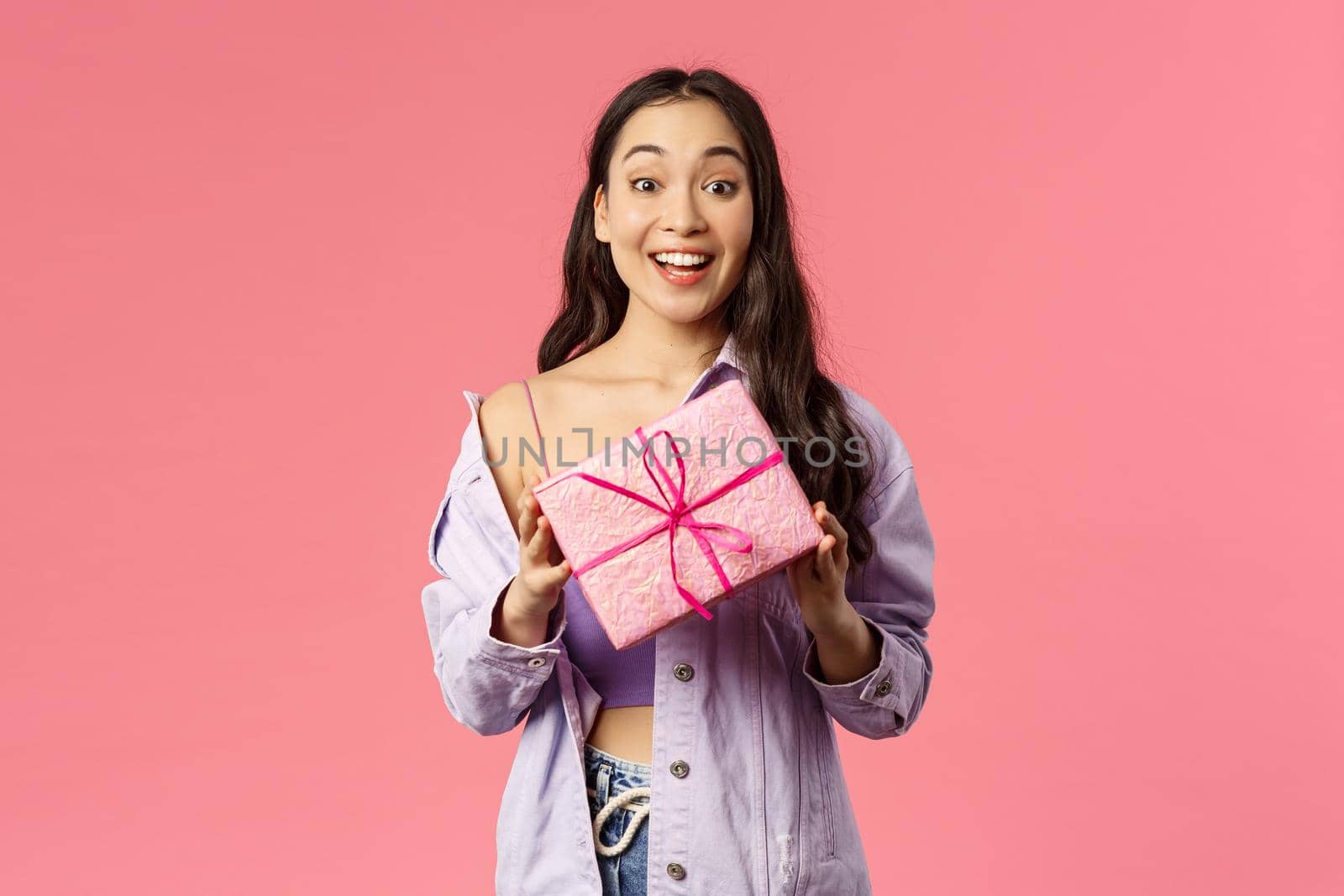 Got present for you. Excited happy young asian girl holding wrapped box with gift, congratulating with holiday or birthday, being invited b-day party, standing amused pink background by Benzoix