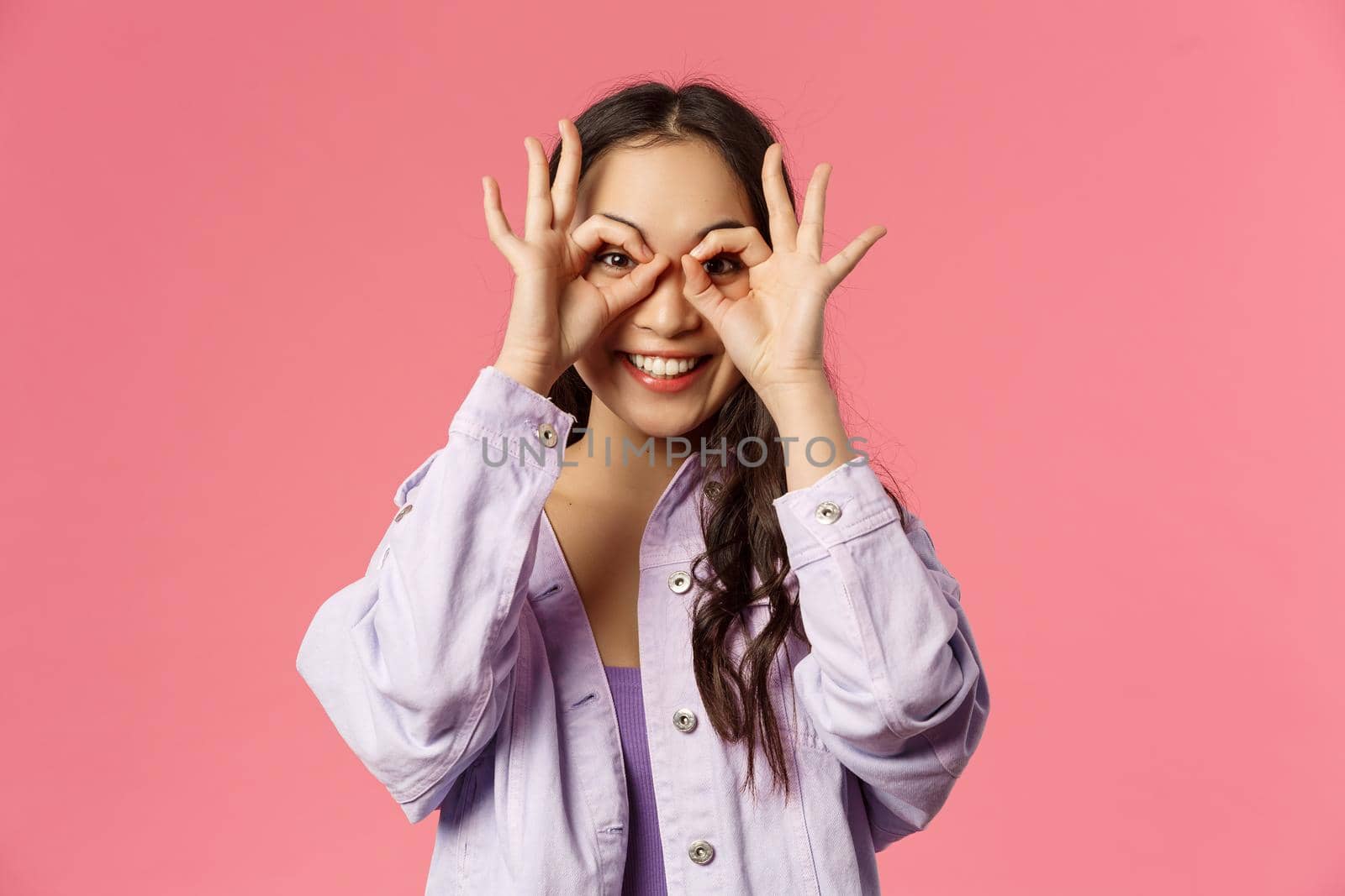 Close-up portrait of charismatic, funny and cute carefree teenage asian girl, making mask with fingers over eyes, smiling and looking camera, having fun, fool around and playing cheerful.