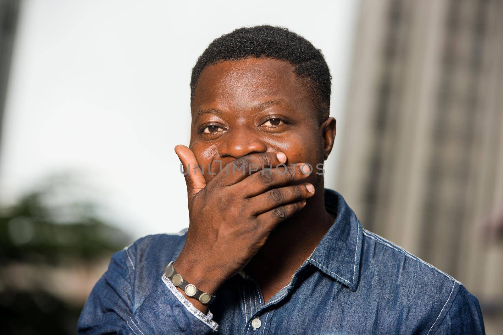 portrait of young man laughing and covering his mouth with the hand trying not to laugh not to offend someone. He just heard a funny joke outside