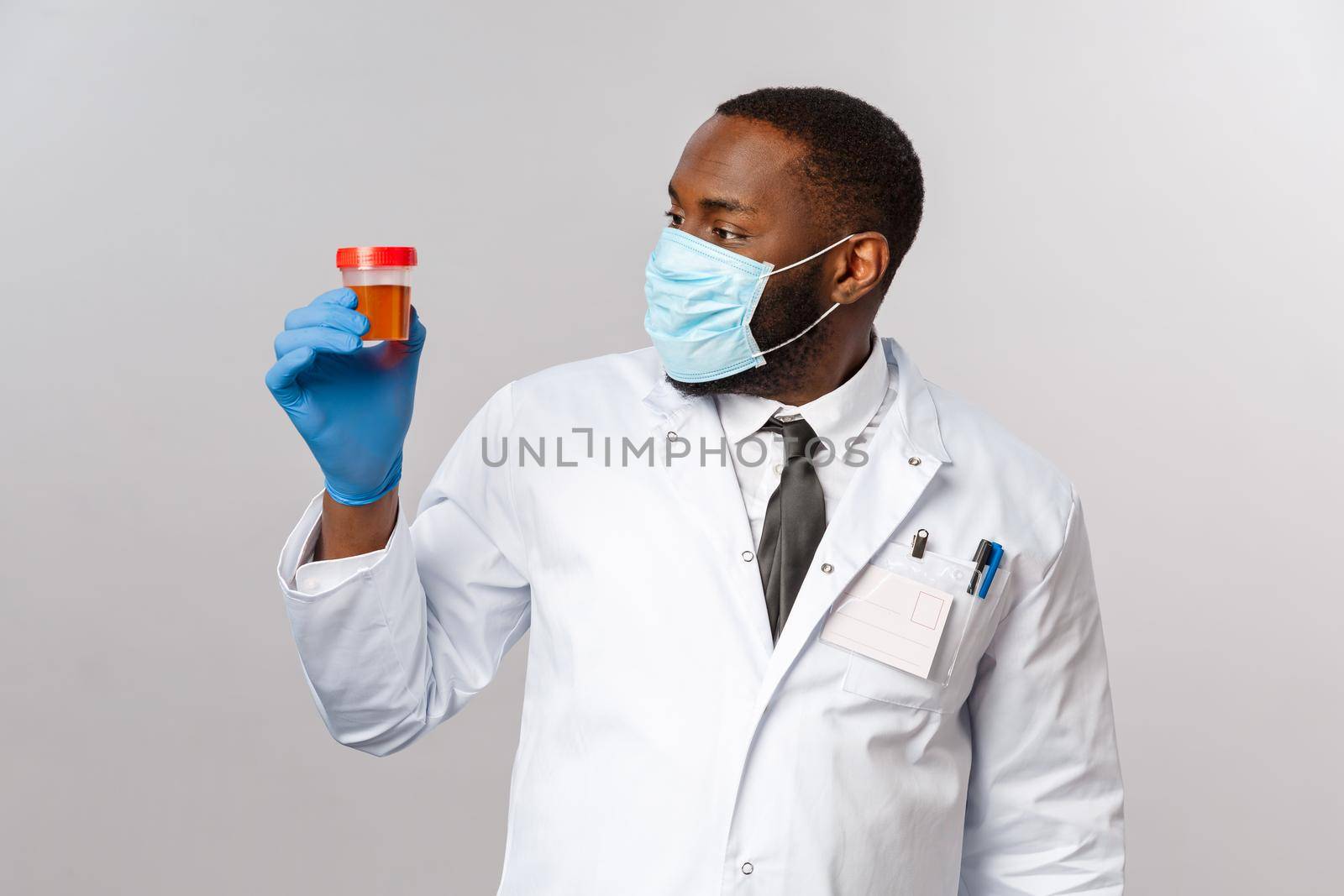 Covid19, pandemic and healthcare concept. Impressed and curious african-american doctor studying patient analysis, looking at urine test with intrigue, wear face mask and medical latex gloves.