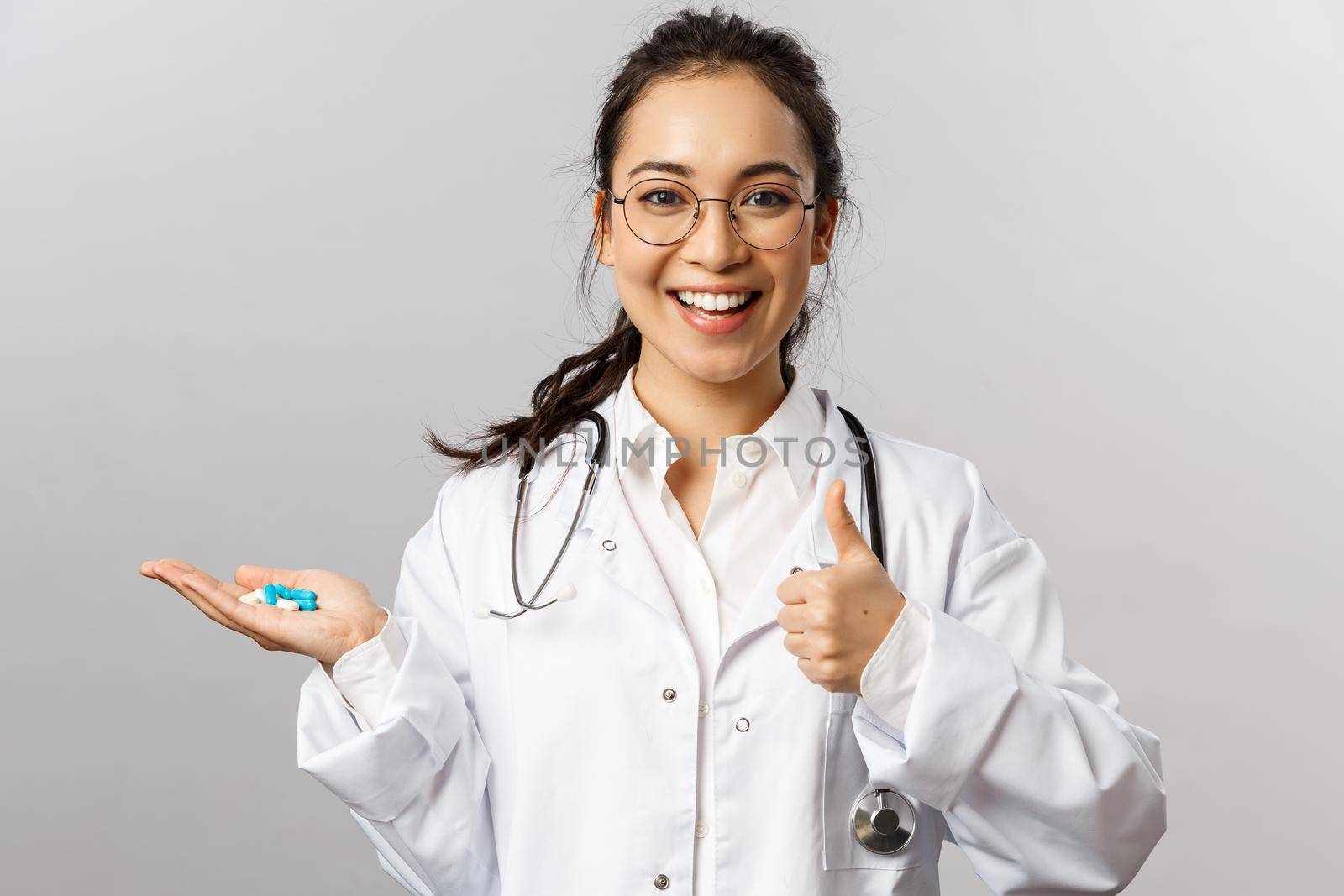 Healthcare, medicine and pharmacy concept. Portrait of upbeat, beautiful asian doctor in white coat, show thumb-up and hold pills, advice take prescribed drugs to cure disease, stay healthy by Benzoix