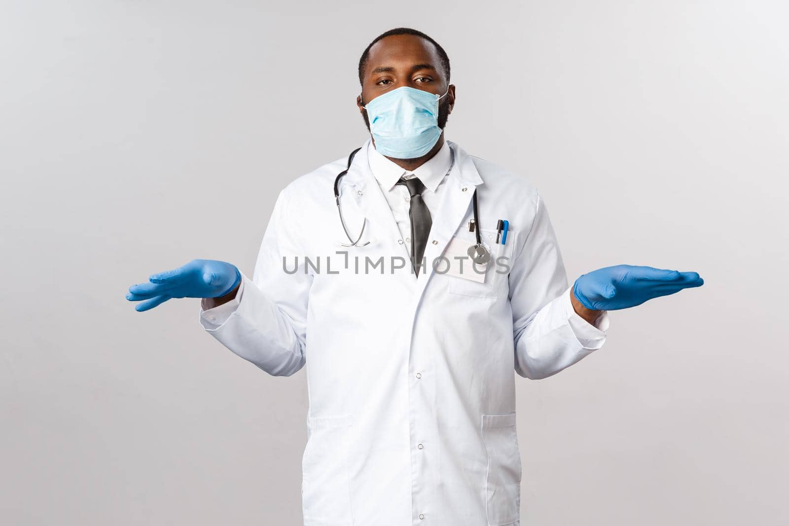 Covid-19, coronavirus patient treatment and disease concept. Tired and bothered african-american doctor in face mask and latex gloves, standing with hands spread sideways prepare for usual check-up by Benzoix