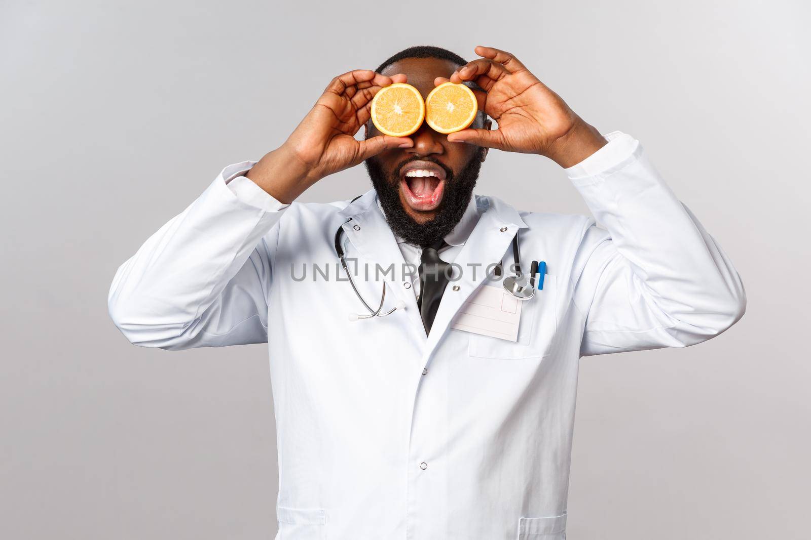 Healthcare, healthy diet and disease concept. Wow so many vitamins. Portrait of amazed happy african-american doctor ask self-distance and eat more vitamins, hold oranges like eyes by Benzoix